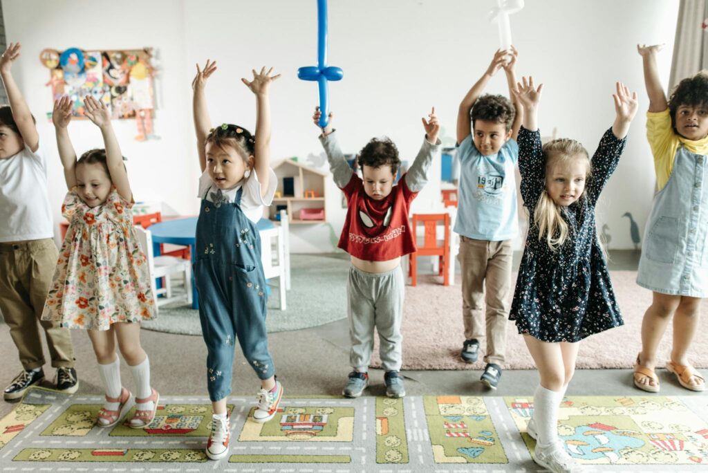 A diverse group of children raising hands while having fun in a lively classroom setting.
